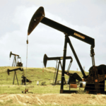 Multiple pumpjack oil rigs operating in a grassy field under a cloudy sky.