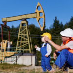 Oil worker and child in safety gear near an oil pumpjack in a rural setting.