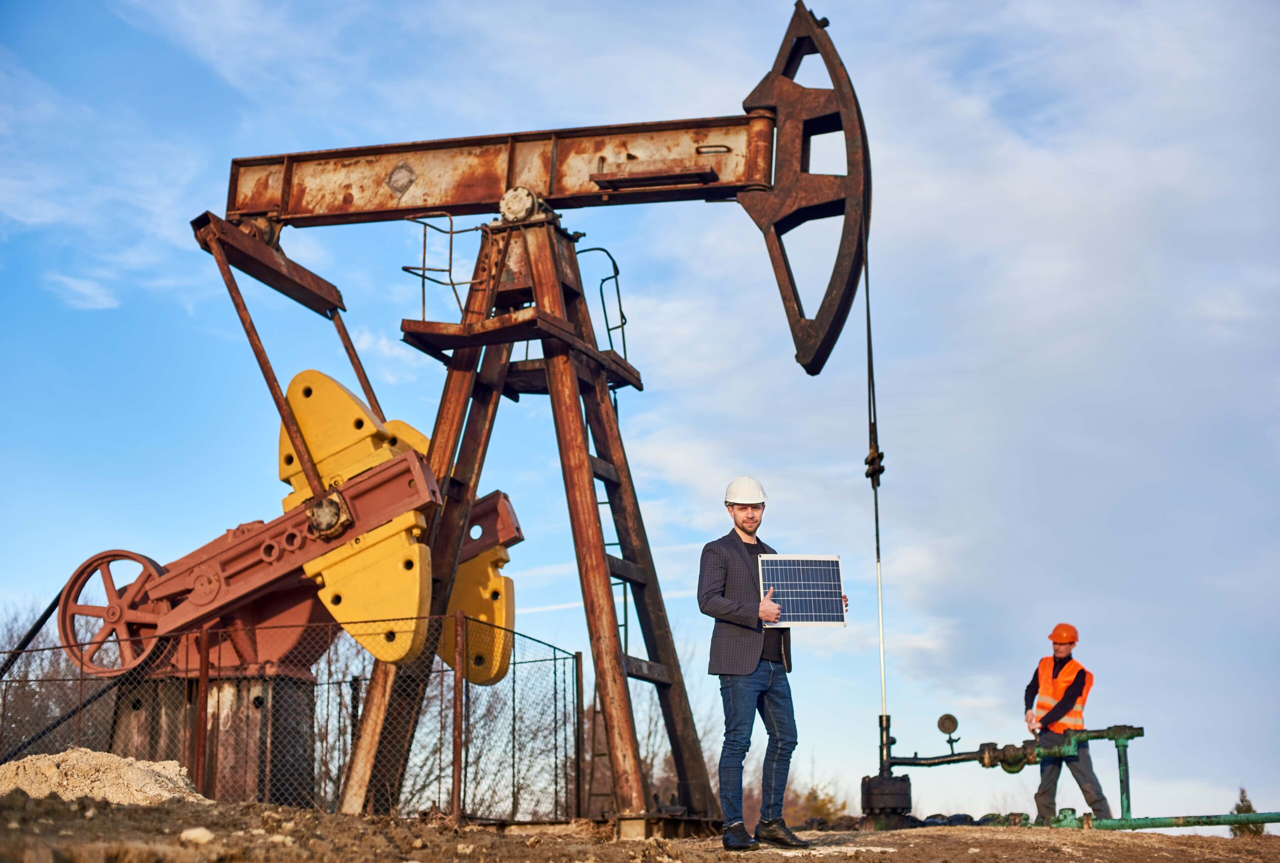 Oil worker in formal attire inspecting an oil pumpjack with a tablet.
