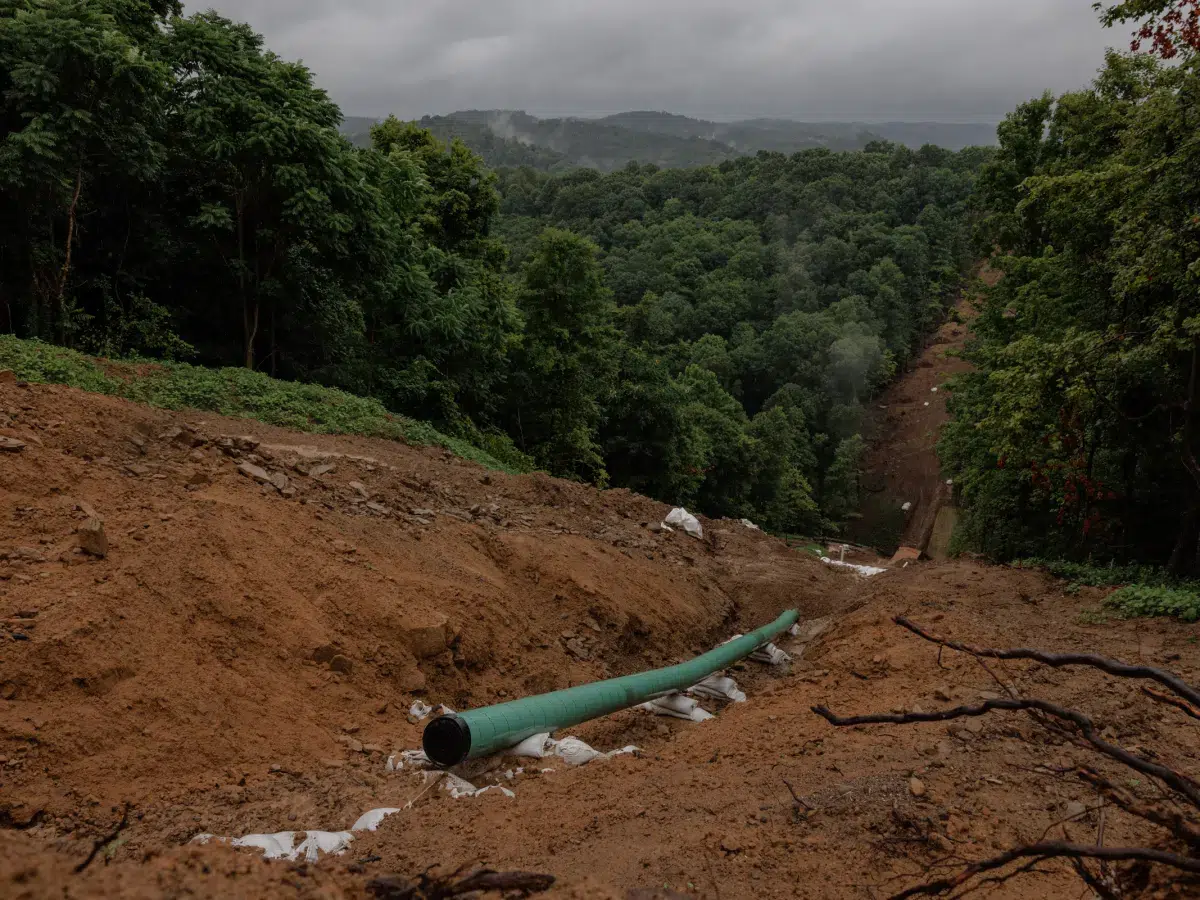 Large green pipeline running through a deforested muddy area in a remote location, likely for oil or gas transport.