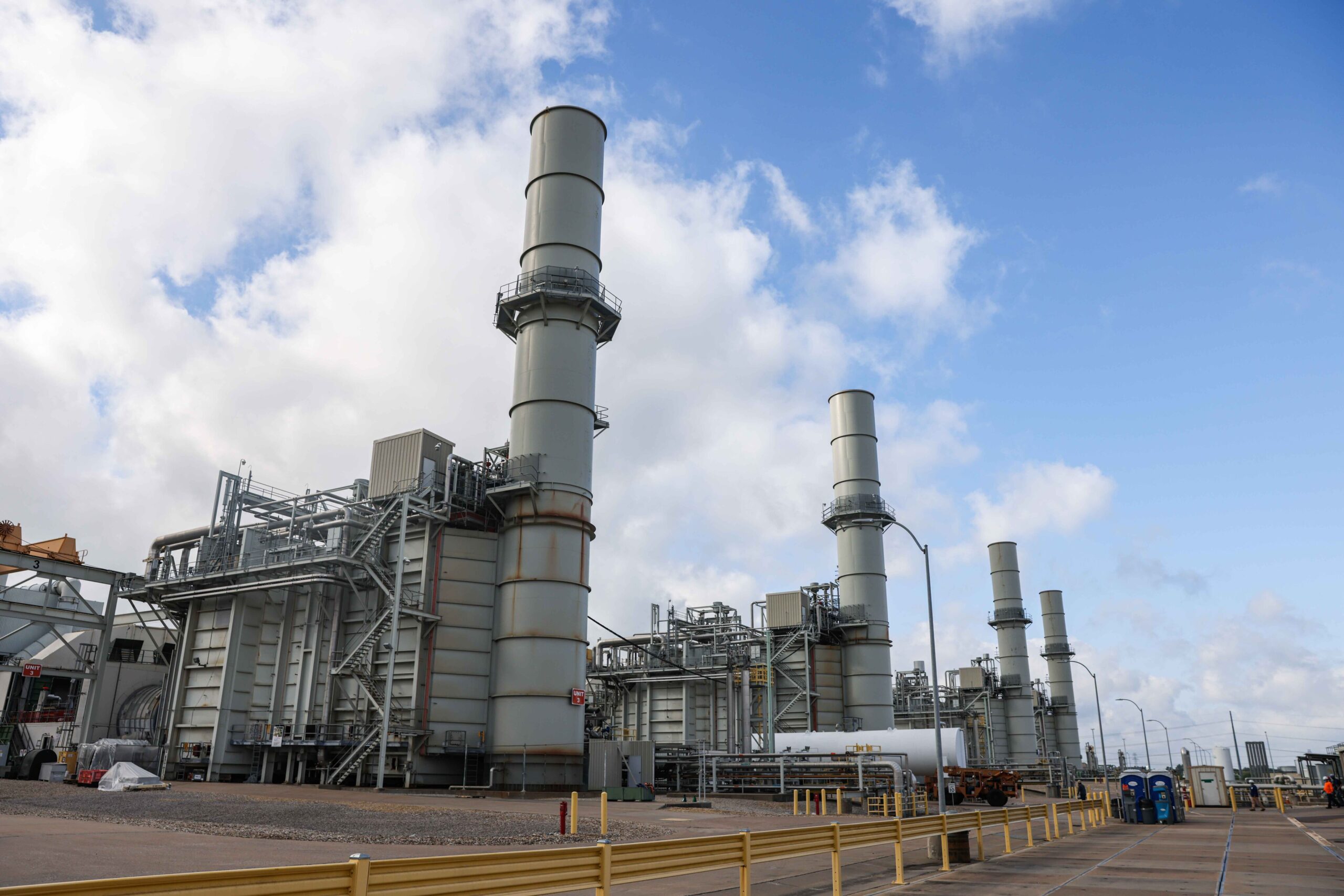 Large industrial power plant with multiple tall smokestacks against a partly cloudy sky.