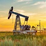 An oil pumpjack in a grassy field during sunset, symbolizing traditional energy sources.