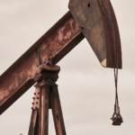 Aging pumpjack oil rig with rusted metal structure under cloudy skies.