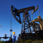 Oil field workers, including a child in safety gear, examining a pumpjack under a bright blue sky.