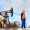 Two oil field workers wearing safety gear discuss operations near a pumpjack under a clear sky.