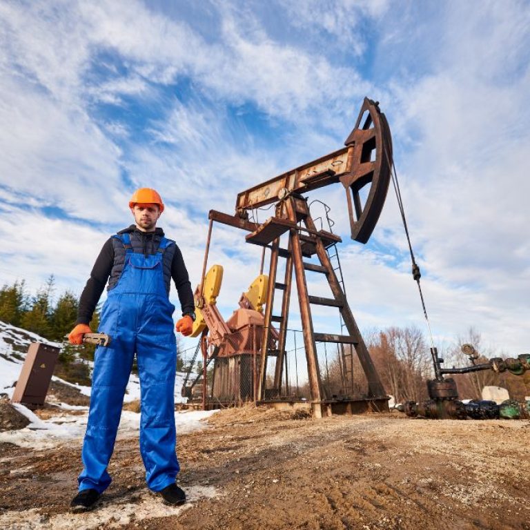 A tall oil drilling rig standing in a grassy field under a clear sky.
