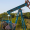 Blue oil pumpjack operating in a rural area with rolling hills and greenery in the background.