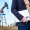 Businessman holding a clipboard and safety helmet with an oil pumpjack in the blurred background