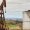 Rusty oil pumpjack and large storage tank in a remote oil field with rolling hills in the background.