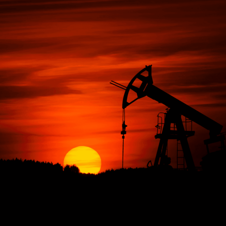Silhouette of an oil pumpjack against a dramatic red sunset sky.