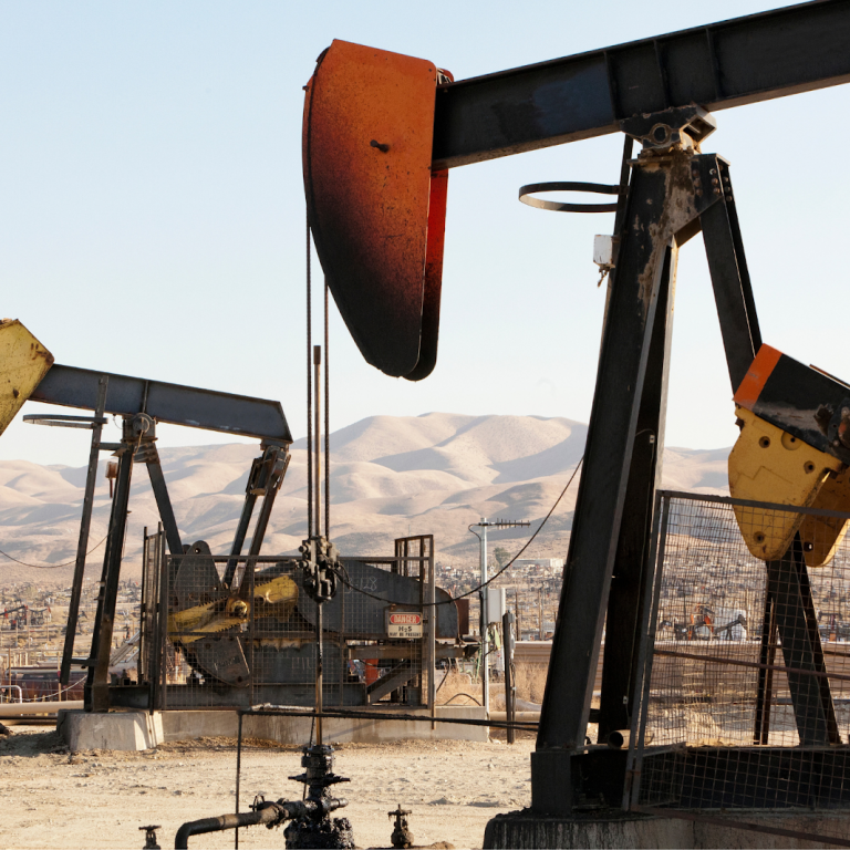 Multiple pumpjack oil rigs operating in a dry landscape with mountains in the background.