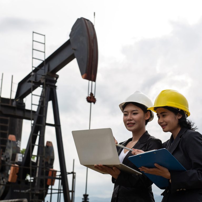 Two female engineers stand beside working oil pumps with a white
