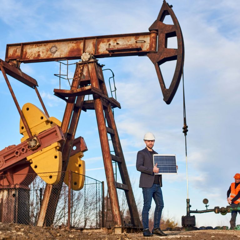 Oil worker in formal attire inspecting an oil pumpjack with a tablet.